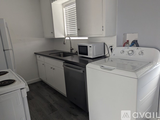 A white washing machine sits in a kitchen with a microwave and oven.