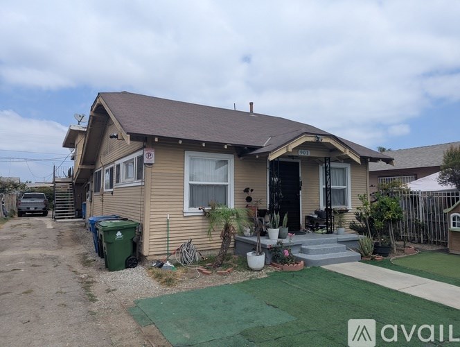 A house with a brown roof and beige siding is surrounded by a gravel driveway and a green lawn.