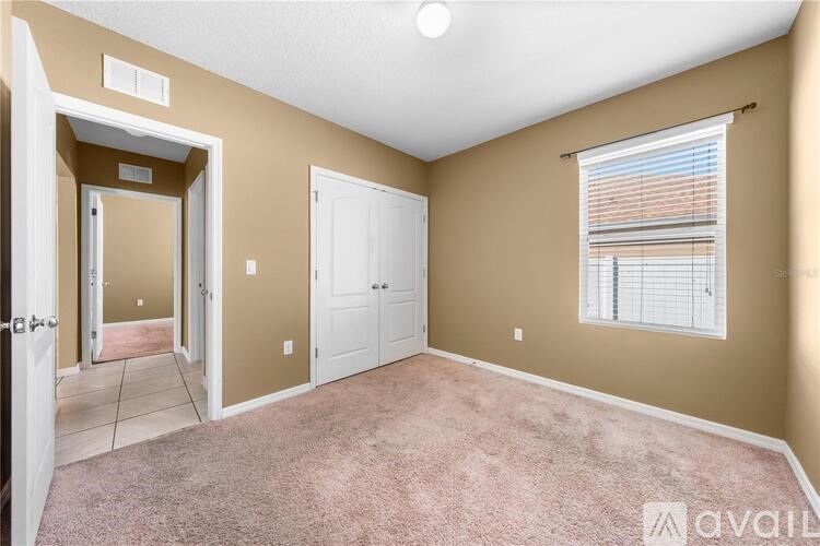 A room with a carpeted floor, a window with blinds, and a door leading to another room.