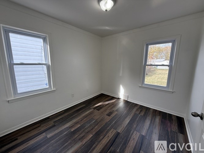 A room with wooden flooring and two windows.