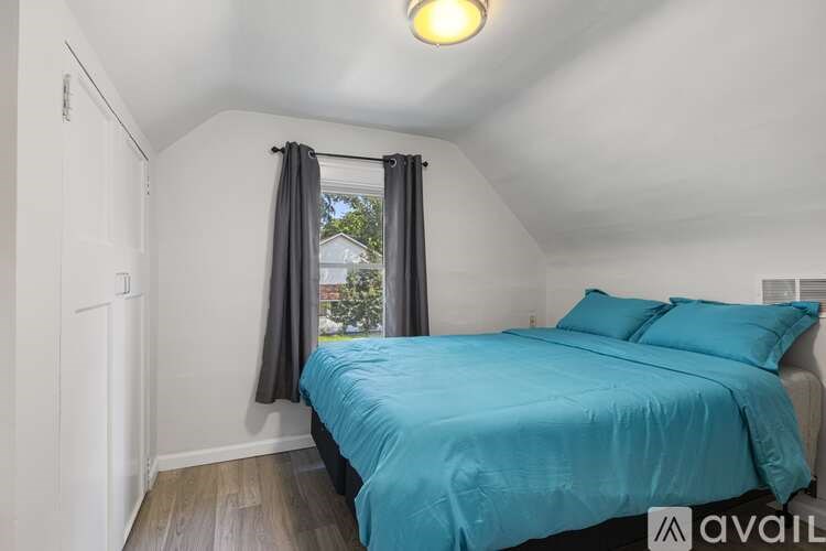A bedroom with a blue bedspread and a window with curtains.