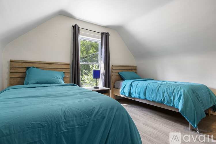 Two beds with blue bedspreads in a room with white walls.