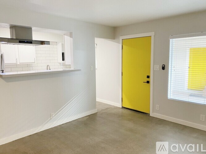 A yellow door is in a white room with a window.