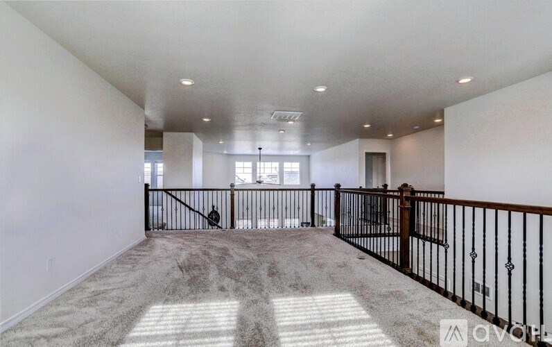 A spacious living room with a carpeted floor and a black railing.