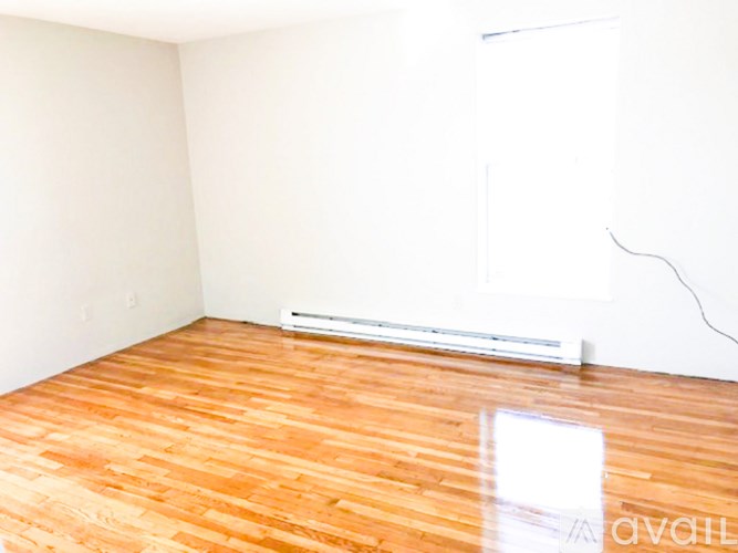 A room with a wooden floor and a white wall with a radiator.