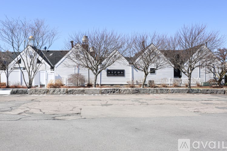 A white house with a black roof and a sign that says "For Sale" in front of it.