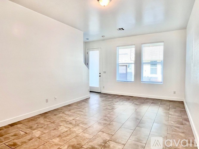 A spacious room with a door, two windows, and tiled flooring.