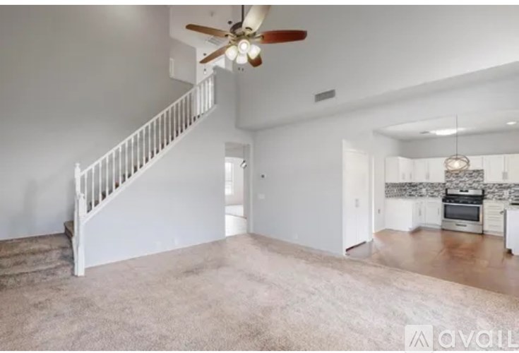 A spacious living room with a staircase and a kitchen area in the background.