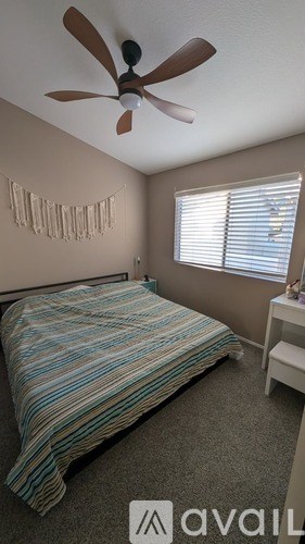 A bedroom with a bed, a fan, and a window with blinds.