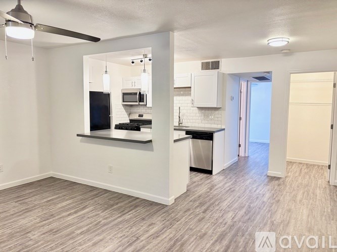 A well-lit, empty kitchen and living room with a ceiling fan.