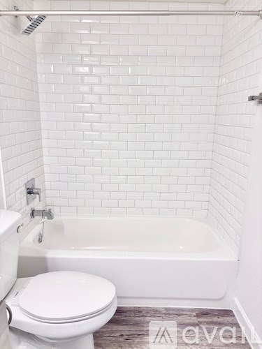 A white toilet sits next to a white bathtub in a white tiled bathroom.
