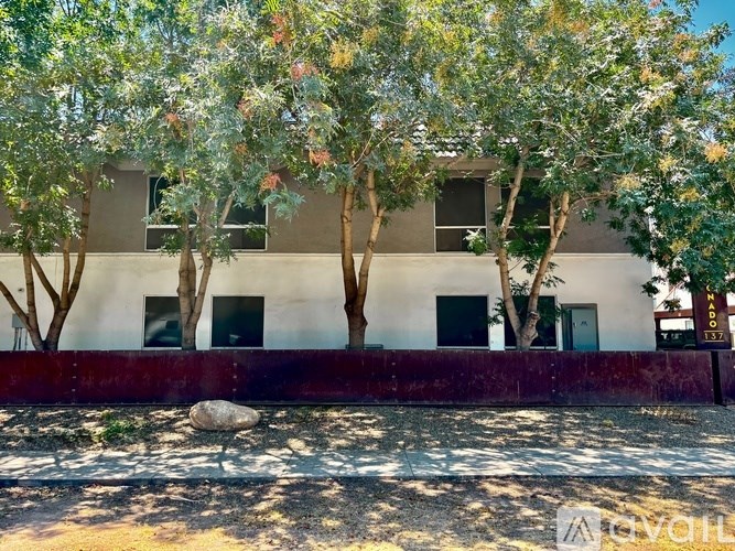 A white building with a red border and trees in front.