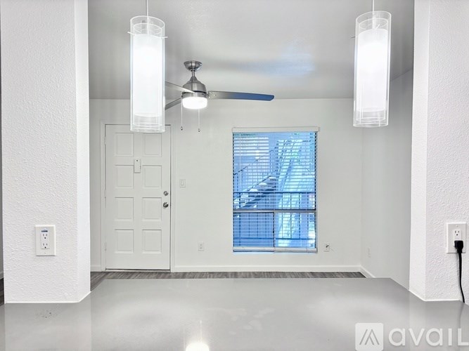 A room with a ceiling fan, two light fixtures, and a window with a view of a balcony.