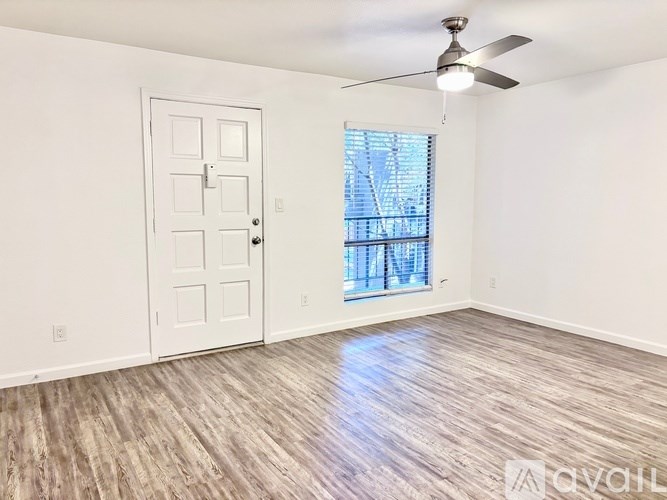 A room with a white door, a ceiling fan, and a window with blinds.
