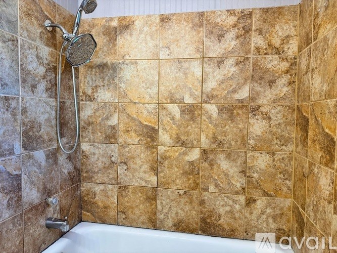 A shower with a brown tile wall and a white tub.