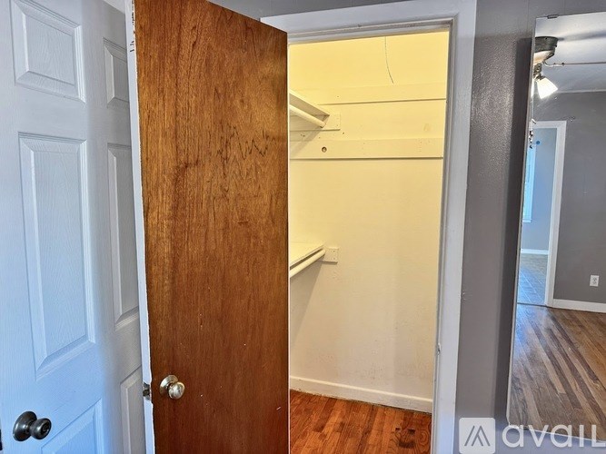 A white door with a black handle is open to a room with a wooden floor and a white wall.