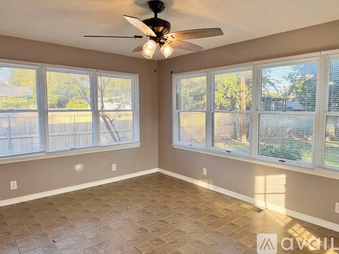 A room with a ceiling fan and large windows.