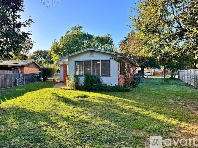 A small white house with a red roof is surrounded by a green lawn and trees.