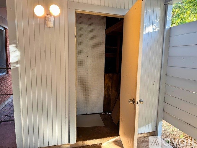 A white wooden shed with a door open to a dark interior.