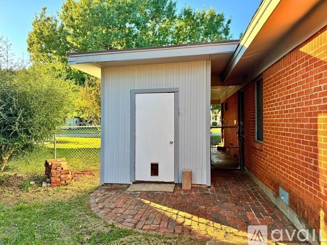 A small building with a white door is surrounded by a brick walkway.