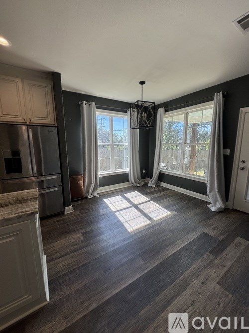 A kitchen with a refrigerator, a window with curtains, and a wooden floor.