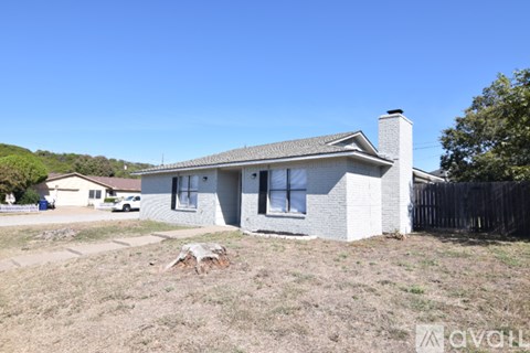 A house with a white exterior and a brown roof is surrounded by a fence and has a clear blue sky above it.