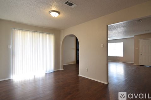 A spacious room with wooden floors and a large window with white curtains.