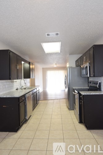 A kitchen with black cabinets and appliances, a white counter, and a tiled floor.