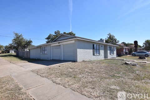 A house with a white exterior and a grey roof is surrounded by a grassy area and a sidewalk.