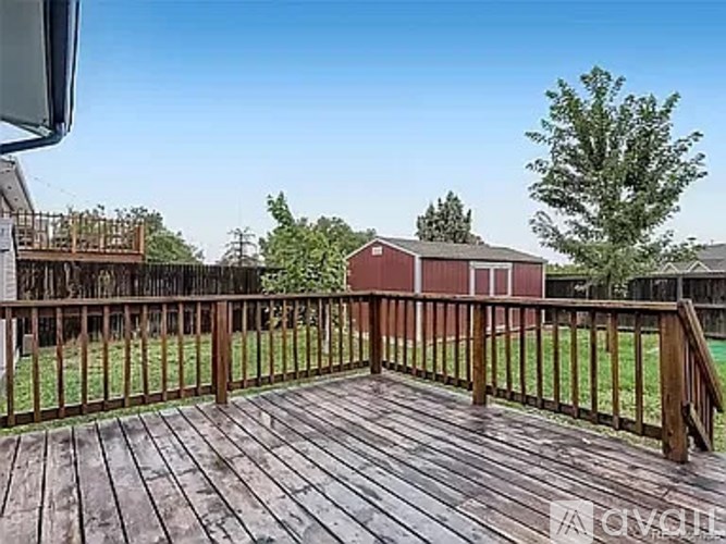 A wooden deck with a railing and a red building in the background.