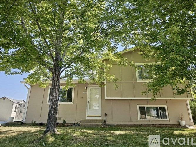 A beige house with a tree in front of it.