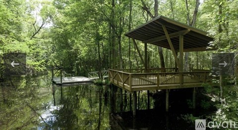 A wooden gazebo is situated in the middle of a lake surrounded by trees.