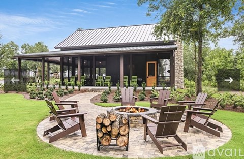 A patio with a fire pit and chairs is surrounded by a grassy area.