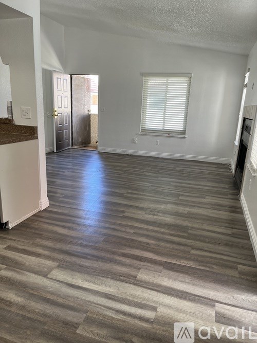 A spacious room with wooden flooring and a window with blinds.
