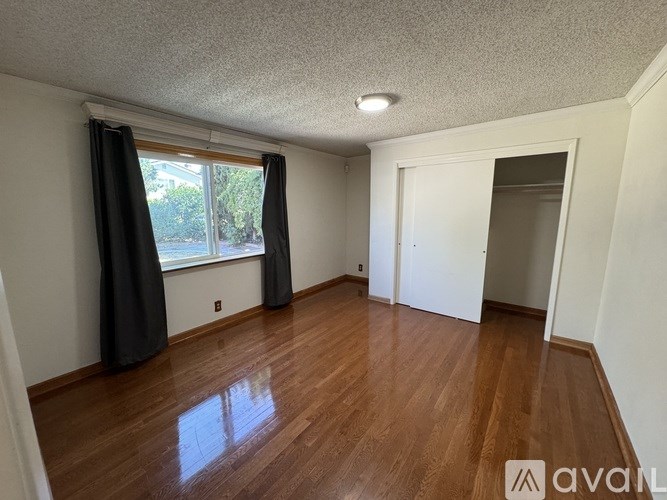 A room with wooden floors and a window with curtains.