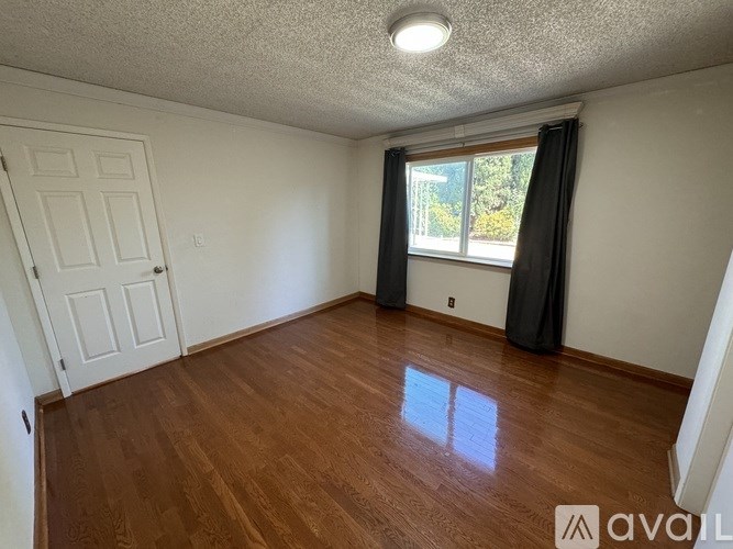 A room with wooden flooring and a window with curtains.