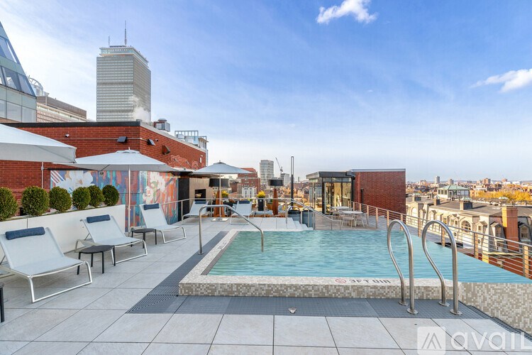 A rooftop pool area with lounge chairs and a city skyline in the background.