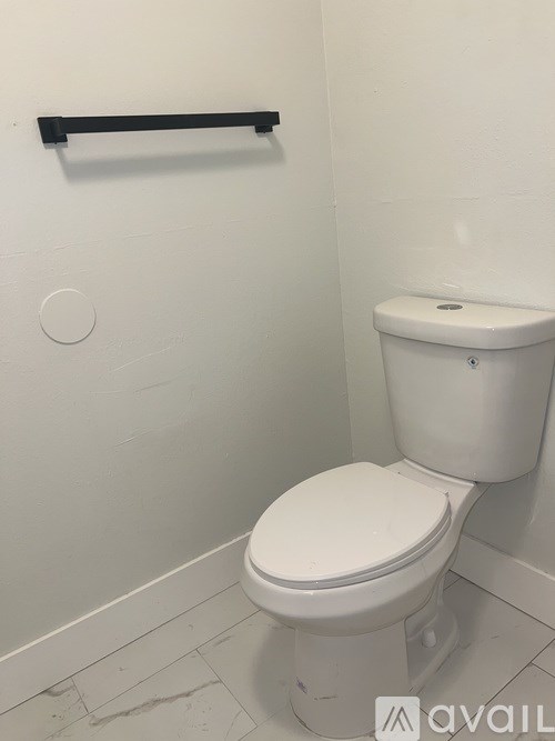 A white toilet in a small bathroom with a black towel bar on the wall.