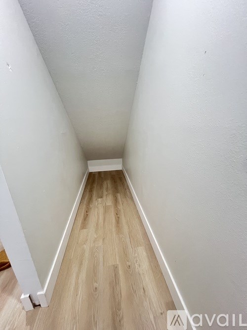 A narrow hallway with wooden flooring and white walls.
