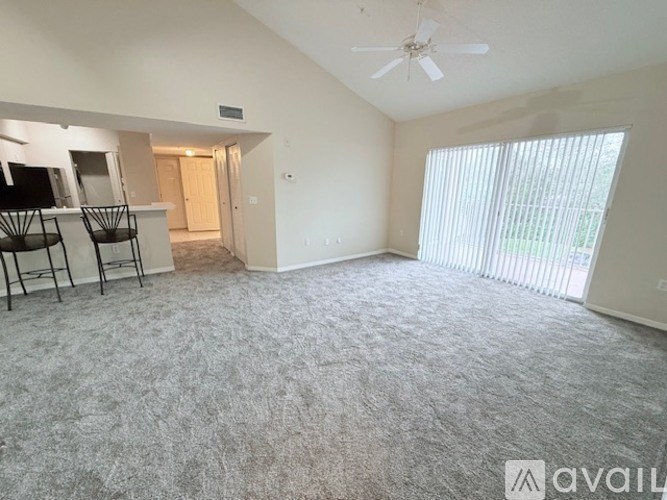A spacious room with a grey carpet and a ceiling fan.