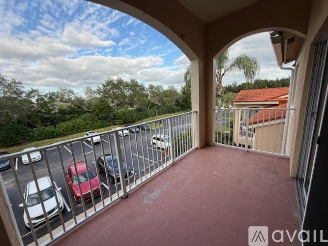 A balcony with a red carpet and a metal railing overlooks a parking lot and trees.