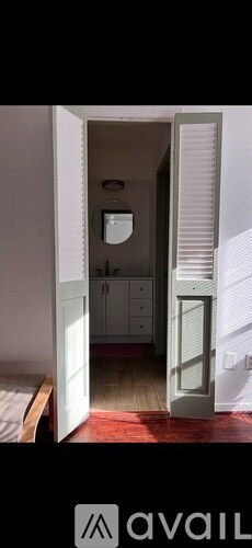 A white door is open to a small room with a bed and a cabinet.