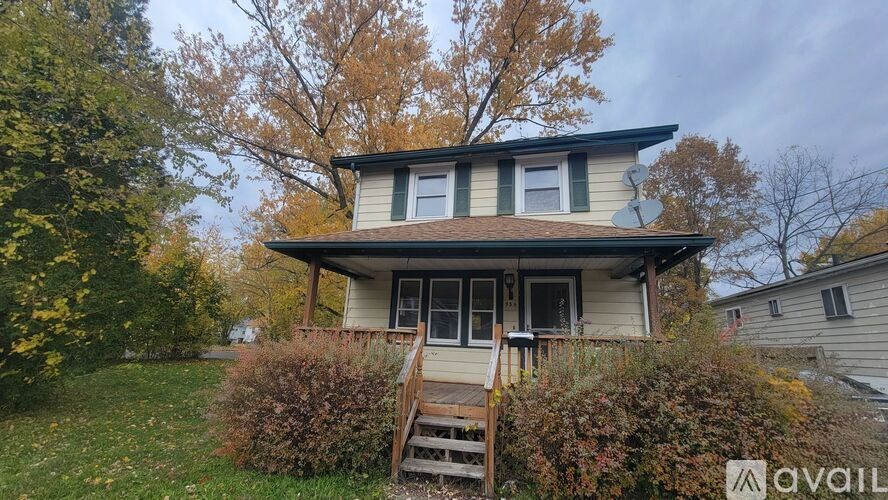 A house with a brown roof and a white wall is surrounded by greenery.