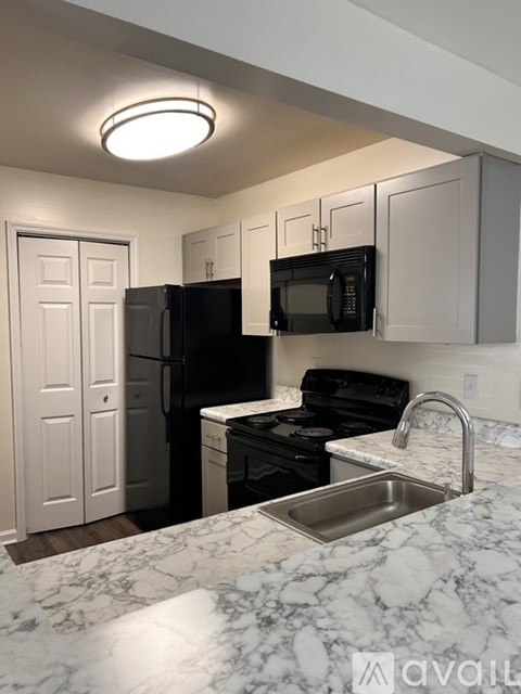 A kitchen with a black fridge and microwave, white cabinets, and a marble countertop.
