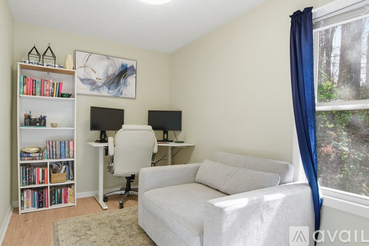 A room with a white couch, a desk with a computer, and a bookshelf filled with books.