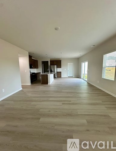 A spacious living room with wooden flooring and a kitchen in the background.