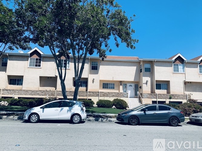 Two cars are parked in front of a building with a tree in the foreground.