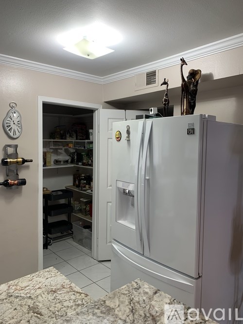 A white refrigerator with a clock on the wall and a small statue on top.
