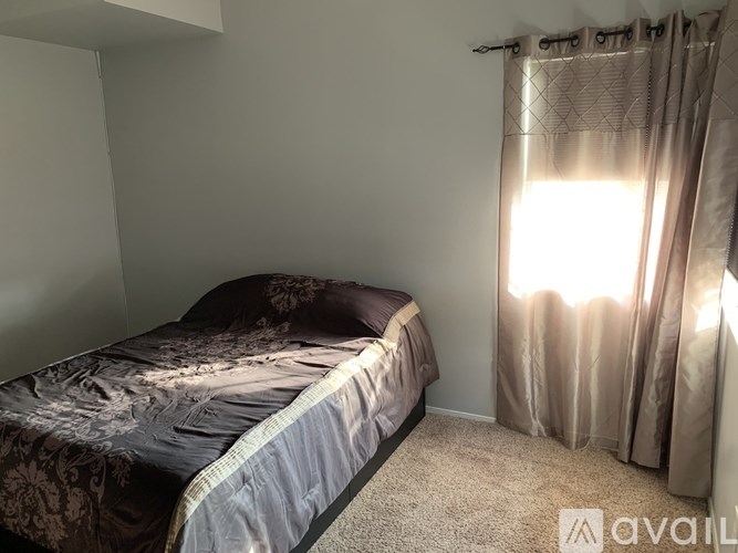 A bedroom with a bed, carpet, and a window with curtains.