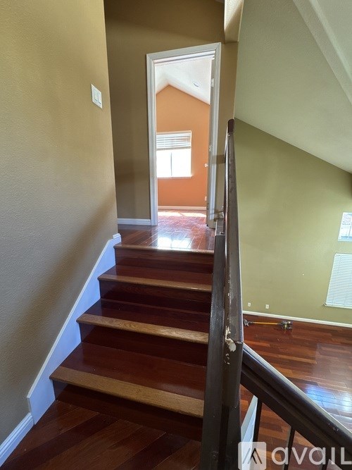 A staircase with a wooden handrail leads to a bright room.